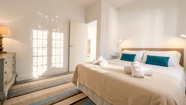 Una habitación de hotel con cama, mesitas de noche, lámpara y vistas al exterior.