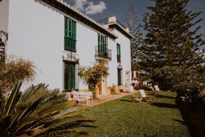 A white building with green shutters, a balcony, and a well-maintained lawn with outdoor seating. - Hacienda Clavero One Garden Apartment (Málaga)