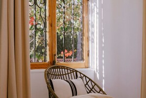 Ein Korbstuhl mit Kissen vor einem Fenster mit Blick auf Bäume und Blumen.