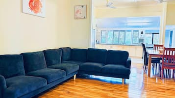 A living room with a dark-colored sectional sofa, wooden flooring, and a dining area with a table and chairs.