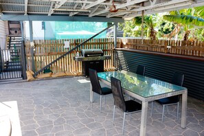 An outdoor patio with a glass-top table and chairs, a barbecue grill, and a wooden fence. - 2- bedroom house in tranquil Rockhampton with Pool (Rockhampton)