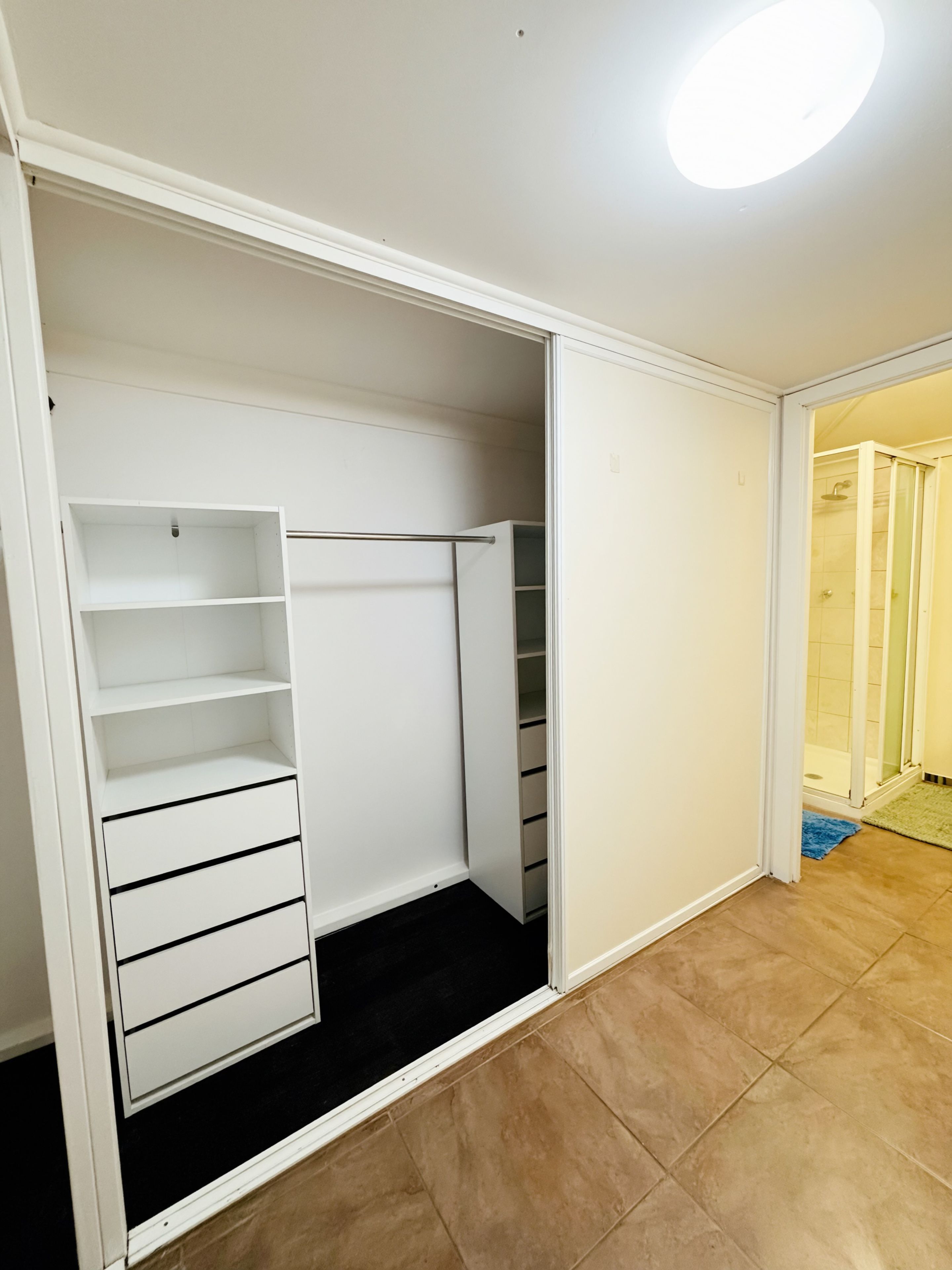 A walk-in closet with open shelves, a hanging rod, and a sliding door leading to a bathroom.