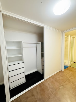 A walk-in closet with open shelves, a hanging rod, and a sliding door leading to a bathroom.
