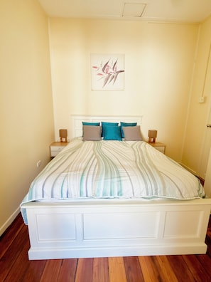 A bed with a striped bedspread, two bedside tables with lamps, a wall-mounted artwork, and a wooden floor.