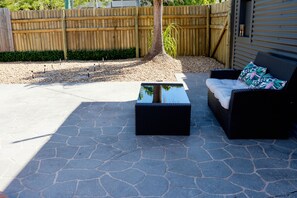 An outdoor patio with a stone floor, a black woven coffee table, and a black wicker sofa with a floral cushion.