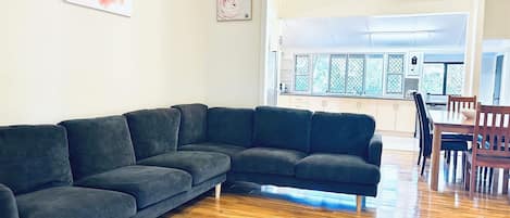 A modern living room with a sectional sofa, wooden flooring, and a view to the dining area.