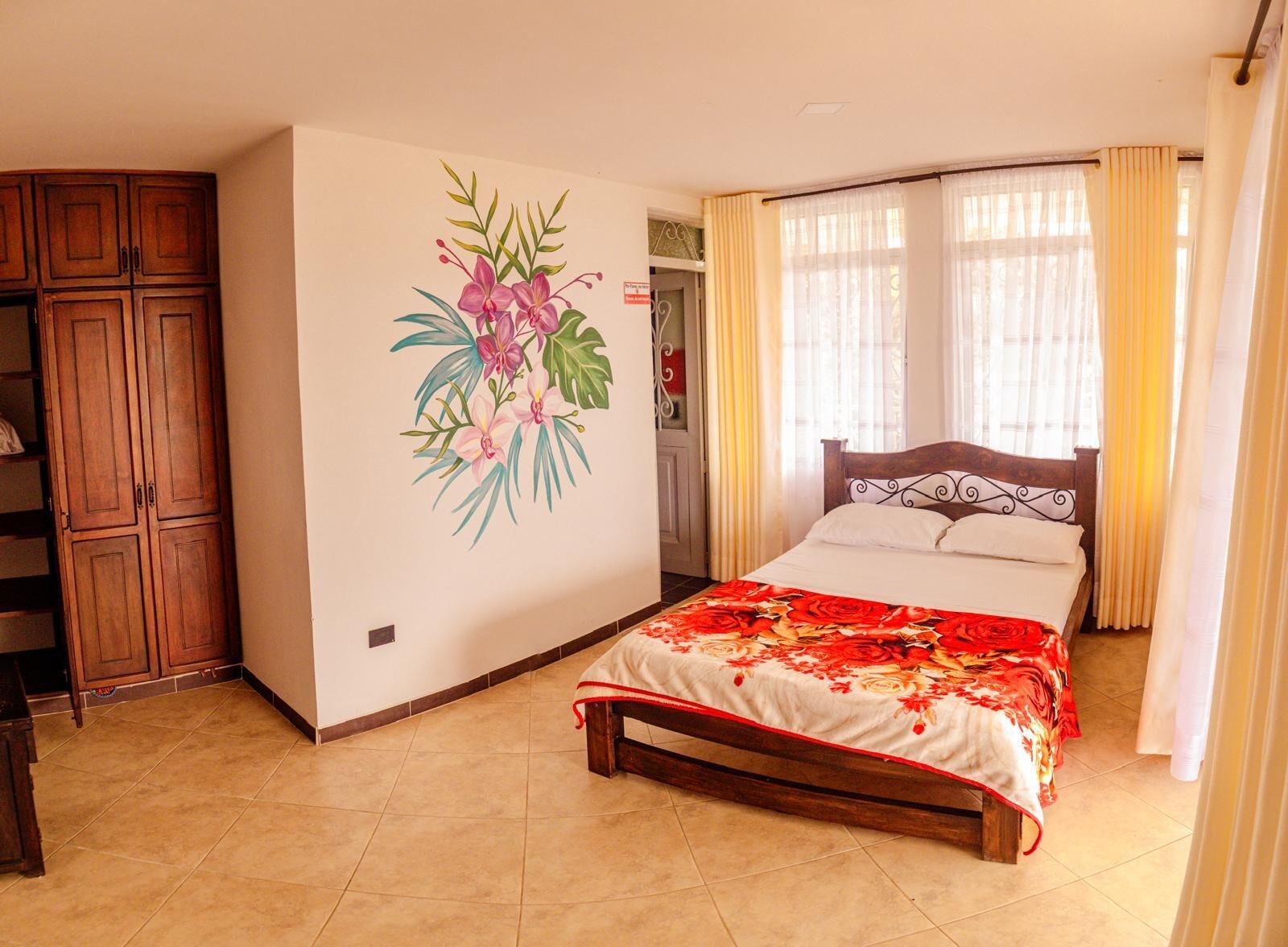Une chambre à coucher comprenant un lit, une armoire et un mur orné d’une fresque à motifs floraux.