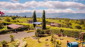 A landscaped garden with a gazebo, a play area, and a view of distant mountains. - Meraki is a Luxury Villa with pool, jacuzzi & Stunning Mountain Views (Quindío)