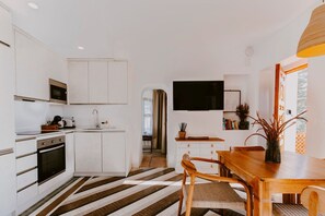 A modern kitchen with white cabinetry, a wooden dining table, and a striped floor. - Hacienda Clavero Two Garden Apartment (Málaga)