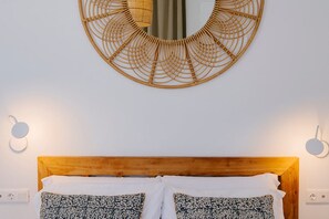 A bed with a wooden headboard, two patterned pillows, a circular wall hanging, and two wall-mounted light fixtures. - Hacienda Clavero Two Garden Apartment (Málaga)