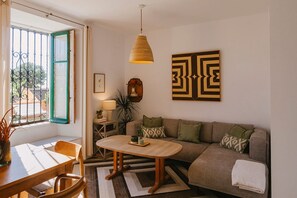 Een woonkamer met een bank, een houten salontafel, een hanglamp, een kunstwerk met geometrische vormen in een lijst, en een raam met uitzicht.