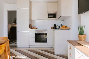 A compact kitchen with white cabinetry, a built-in oven, a microwave, and a coffee maker. - Hacienda Clavero Two Garden Apartment (Málaga)