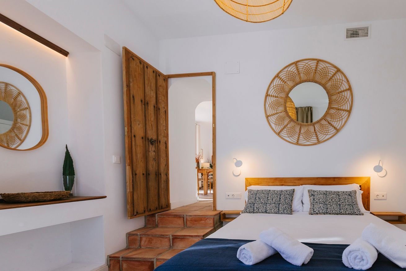 A hotel room with a bed, a wooden wardrobe, a mirror, and a wall-mounted light fixture.