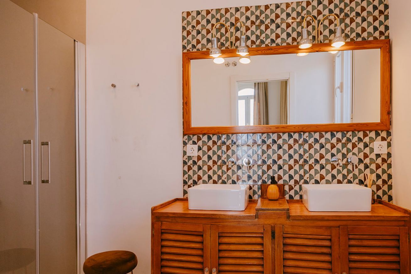 Un bagno con un mobile lavabo in legno, due lavandini, uno specchio con illuminazione e piastrelle decorate.