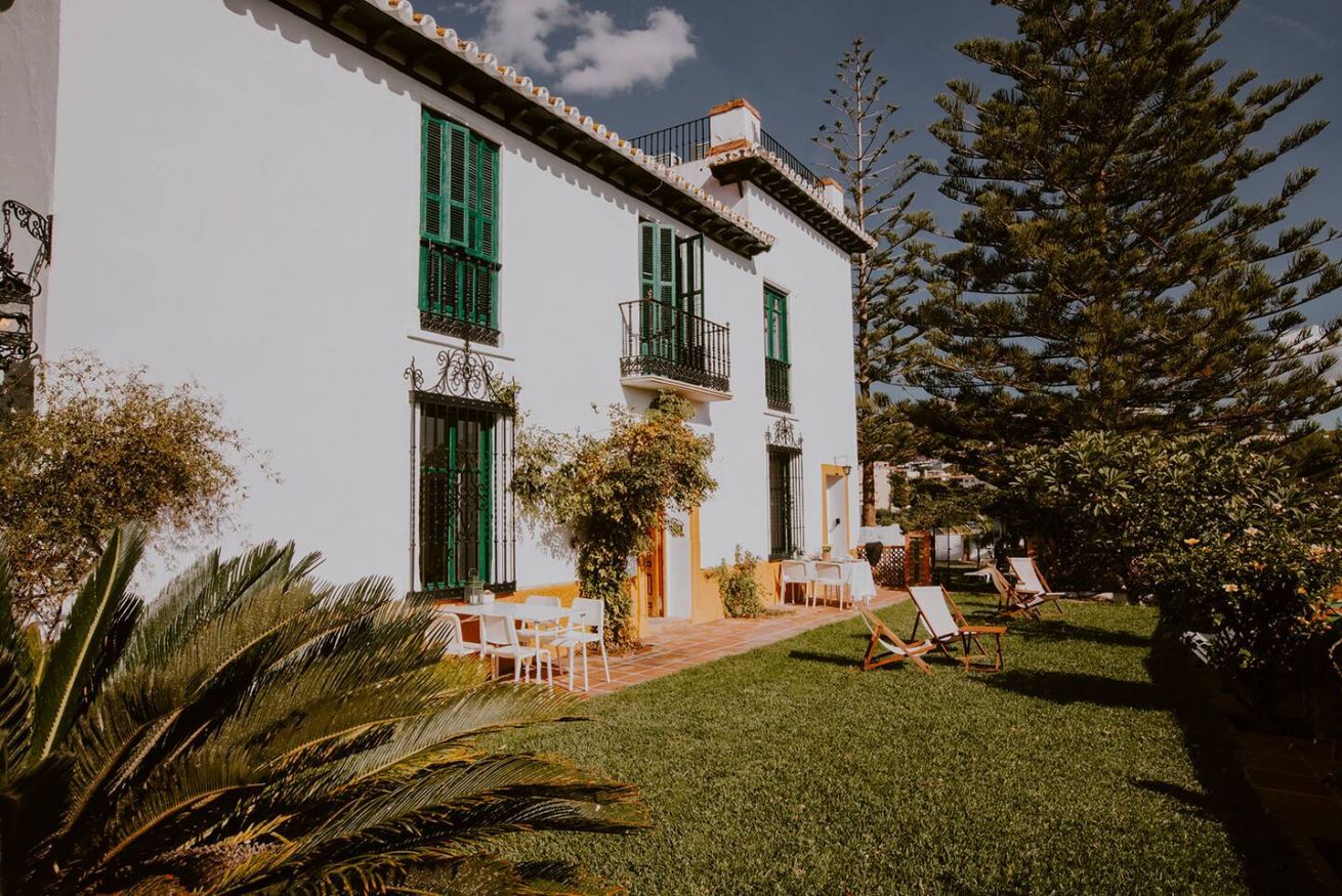Un edificio blanco con contraventanas verdes, un balcón y un césped con sillas.