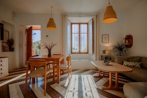 Un coin repas avec une table et des chaises en bois, un banc, un tapis à motifs et une fenêtre avec des rideaux.
