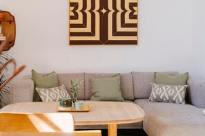 A living room with a sofa, cushions, a round table, and a wall-mounted abstract artwork. - Hacienda Clavero Two Garden Apartment (Málaga)
