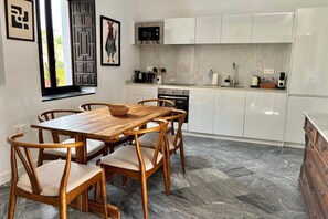 A modern kitchen with white cabinets, a wooden dining table, and a herringbone-patterned floor. - Hacienda Clavero Three Patio Apartment: (Málaga)