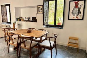 A dining area with a wooden table and chairs, a small wooden bench, and a window with a view of greenery. - Hacienda Clavero Three Patio Apartment: (Málaga)