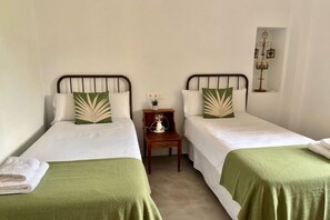 A twin room with two single beds, each with a green bedspread and matching pillows. There is a small wooden nightstand between the beds with a lamp and a small plant. - Hacienda Clavero Three Patio Apartment: (Málaga)