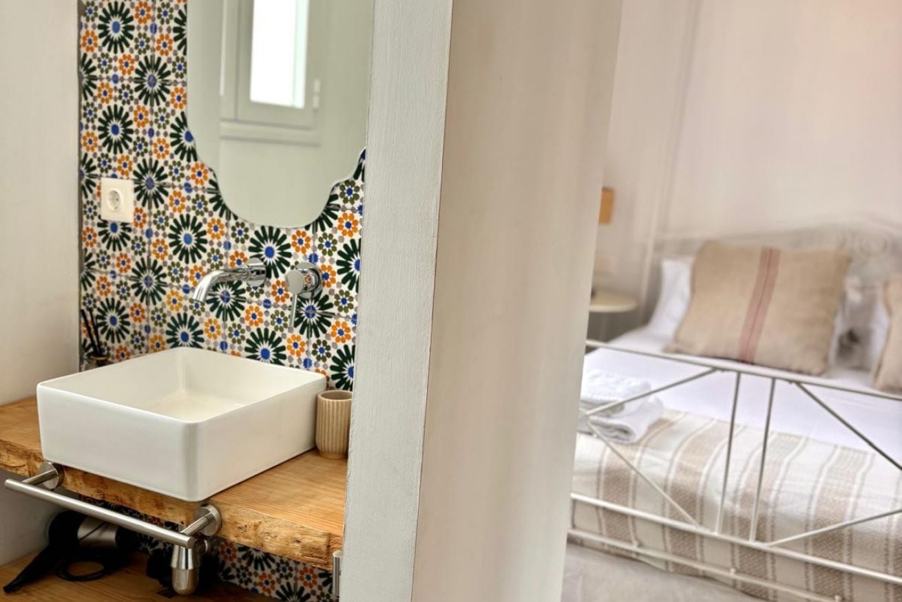 Ein Badezimmer mit einem weißen Waschbecken, einem Spiegel und einer gefliesten Rückwand mit Muster.