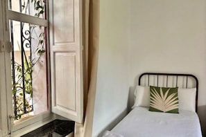 A room with a bed, a window with metal bars, and a door. - Hacienda Clavero Three Patio Apartment: (Málaga)