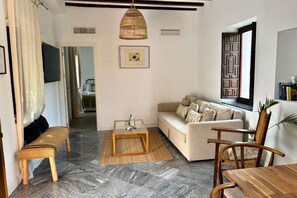 A living room with a sofa, a bench, a coffee table, and a dining table. - Hacienda Clavero Three Patio Apartment: (Málaga)