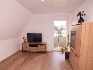 Ein Zimmer mit Fernseher auf einer Holzkommode, einer Topfpflanze und Blick durch eine Glastür.