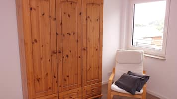 Une pièce avec une armoire en bois, une chaise blanche avec un coussin et une fenêtre donnant sur un beau paysage.