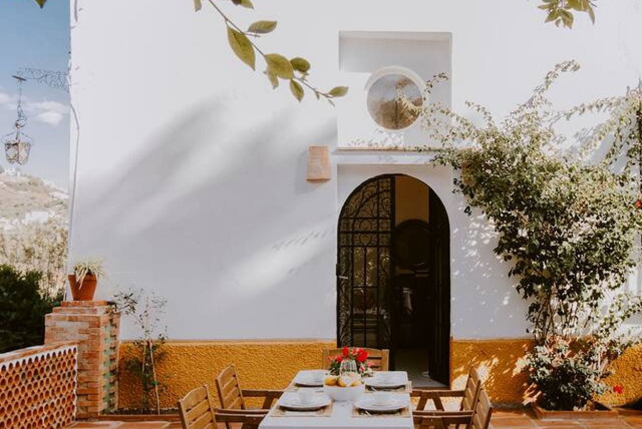 Un espace de restauration en plein air avec une table dressée pour quatre personnes, un mur en briques et une porte dotée d’une entrée en arc de cercle.