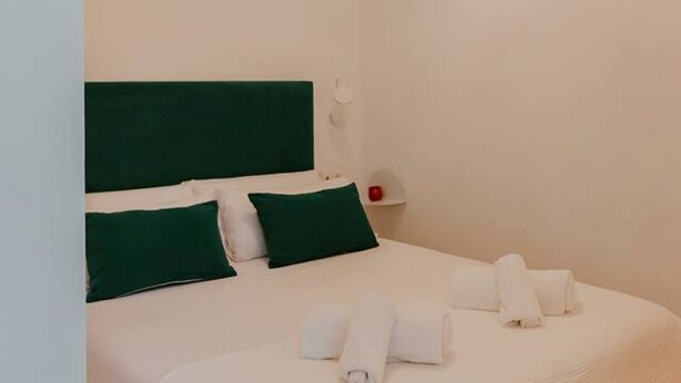 Una cama con cabecera verde, ropa de cama blanca y toallas enrolladas sobre la cama.