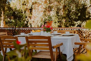 An outdoor dining area with wooden chairs and a table set with white tablecloths, plates, and a centerpiece of flowers. - Hacienda Clavero Four Garden Apartment: (Málaga)