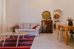 A living room with a sofa, a coffee table, a cabinet, and a dining table with chairs. - Hacienda Clavero Four Garden Apartment: (Málaga)