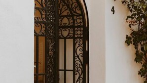 Una reja de hierro forjado con diseños intrincados, una pared blanca con un letrero con el número 4, y una enredadera creciendo en la pared.