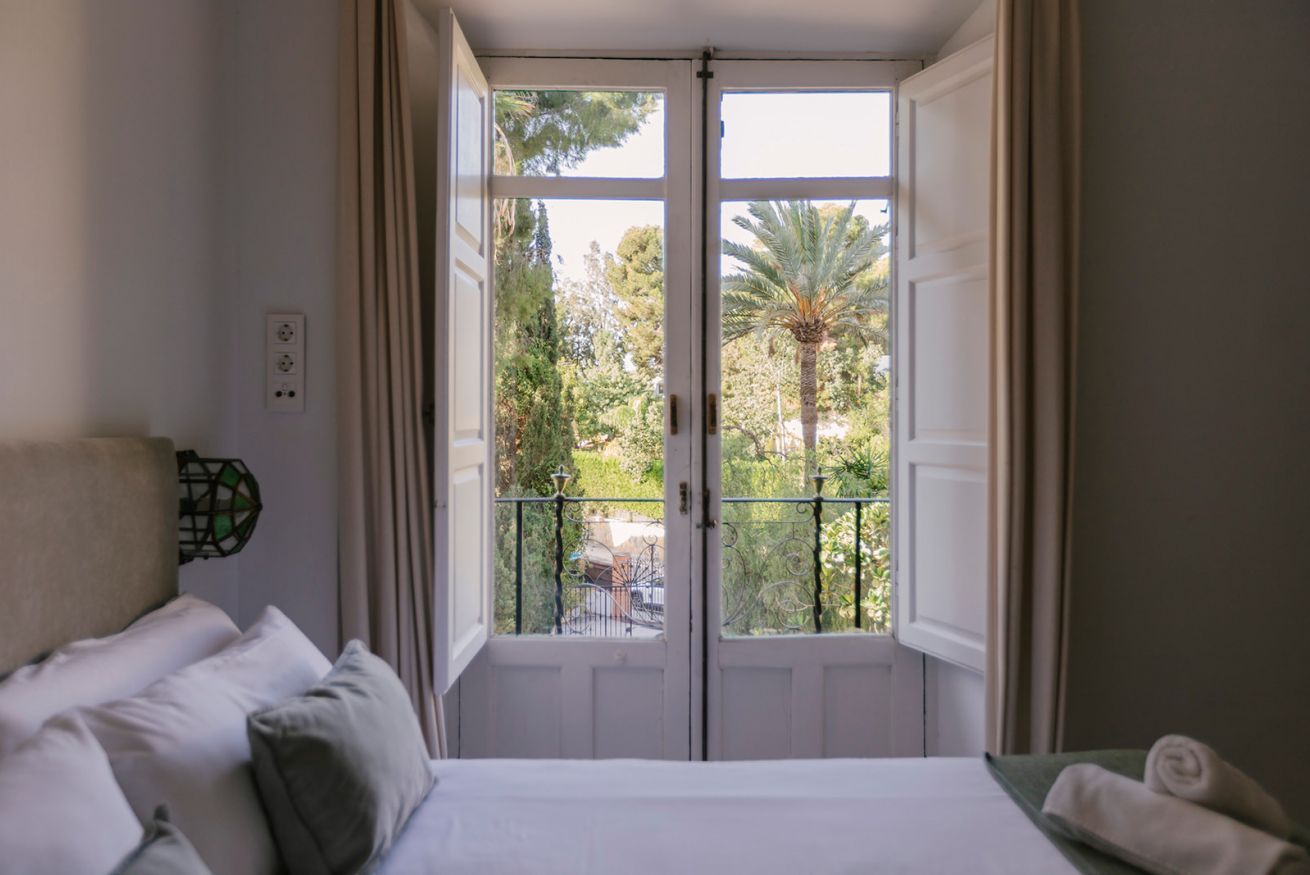 Une chambre à coucher avec un lit, une fenêtre et une vue sur un balcon agrémenté de verdure.