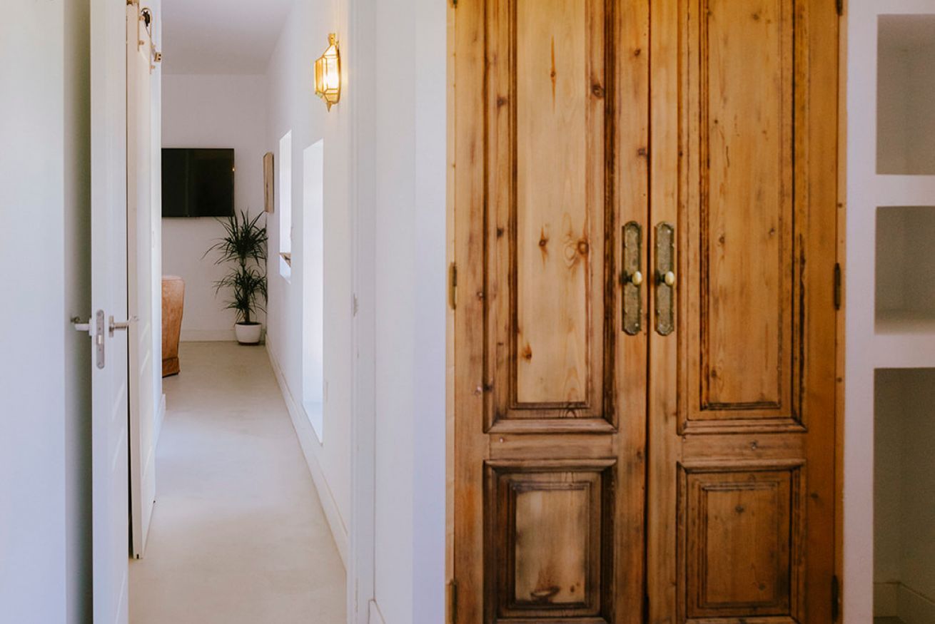 Un couloir avec une porte en bois, une plante en pot et un luminaire fixé au mur.