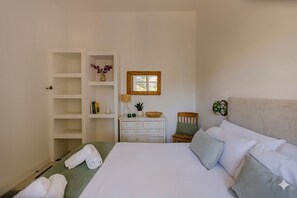 Ein Schlafzimmer mit einem Bett, einer Kommode, einem Sessel, einem Regal mit Dekoration und einem Spiegel an der Wand.