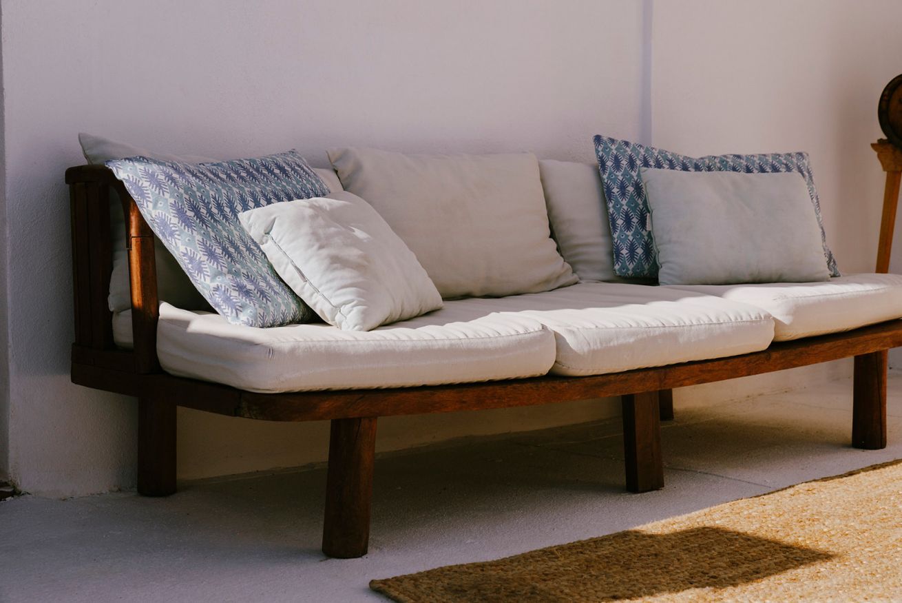 Un banc en bois avec un coussin et un oreiller à motifs, placé contre un mur.