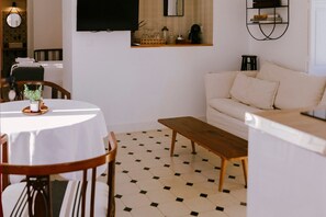 Una sala de estar con un sofá blanco, un banco de madera, una mesa de comedor con sillas y un piso de baldosas.