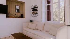 Una sala de estar con sofá, una mesita de centro, estantería empotrada y ventana con contraventanas.