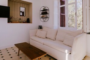 Ein Wohnzimmer mit Sofa, Couchtisch, Wandregal und einem Fenster mit Rollläden.