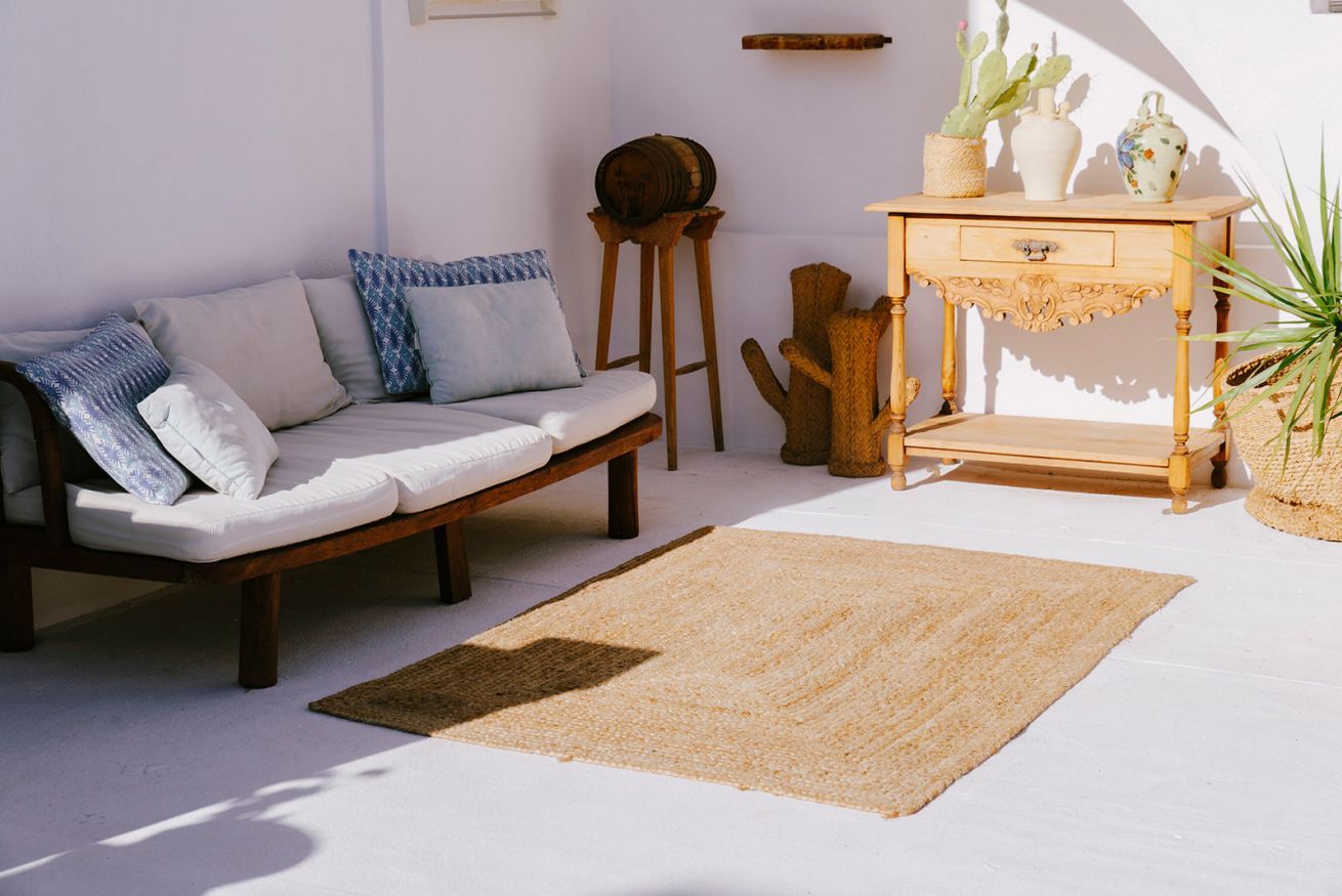 Een kamer met een bank, een klein houten tafeltje met lade, een cactus en een geweven vloerkleed.