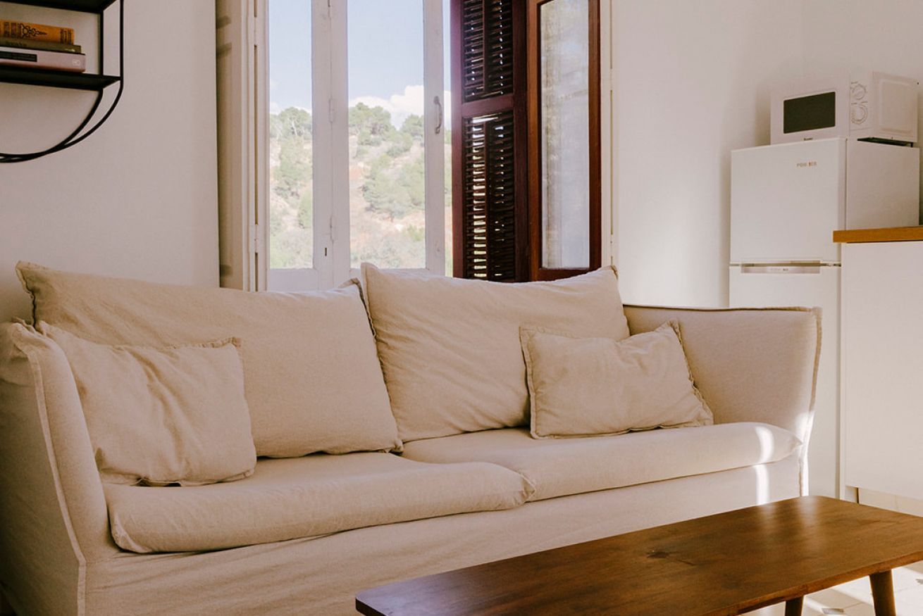 Una sala de estar con un sofá color beige, una mesa de centro de madera y un refrigerador blanco.