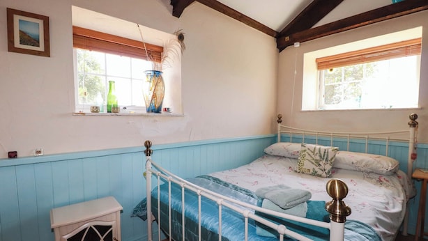 Un dormitorio con cama, mesita de noche, ventana con cortinas e imagen en la pared.