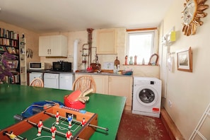 A compact kitchen with a washing machine, a table with a foosball table, and a window with a view.
