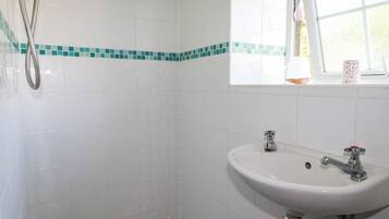 Un baño con azulejos blancos, ducha, lavabo y ventana con vistas.
