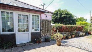 Una casa con una puerta blanca, un muro de piedra y un jardín con plantas en macetas.