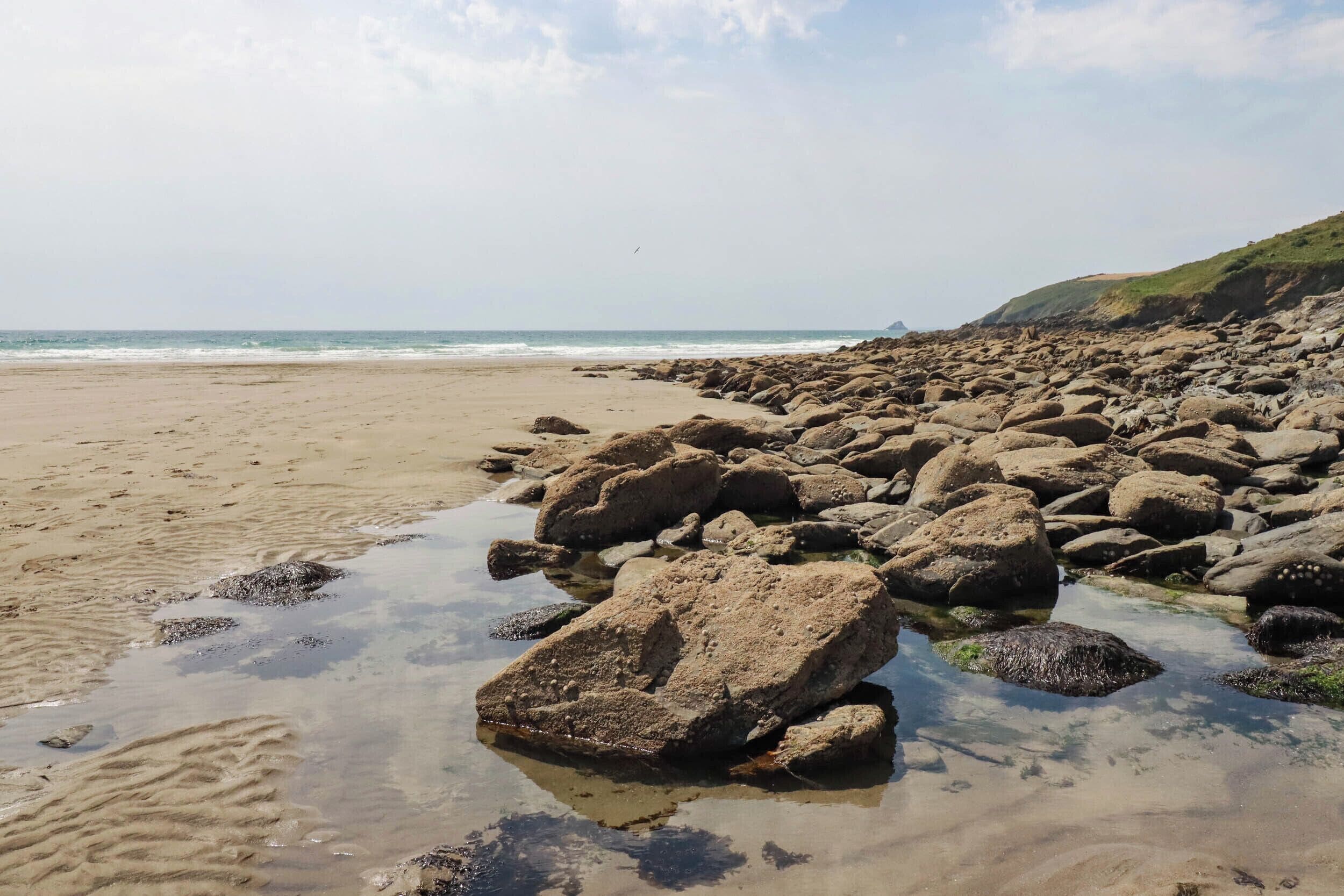 A rocky beach with clear water and a distant view of the sea.