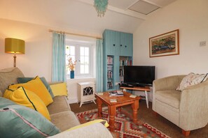 A living room with a sofa, a coffee table, a television, and a bookshelf. - The Granary (Truro)