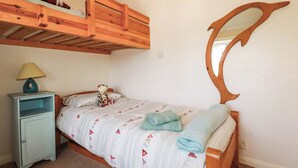 A bedroom with a bunk bed, a bedside table with a lamp, a bed with a patterned duvet, and a wall-mounted mirror. - The Granary (Truro)